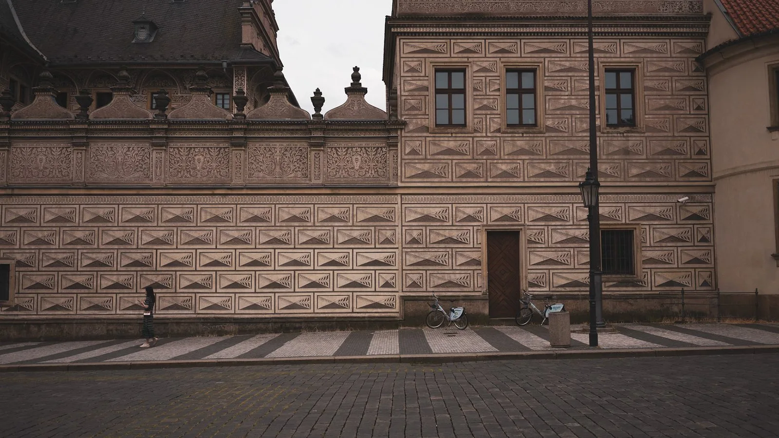 A lone figure beside a patterned wall